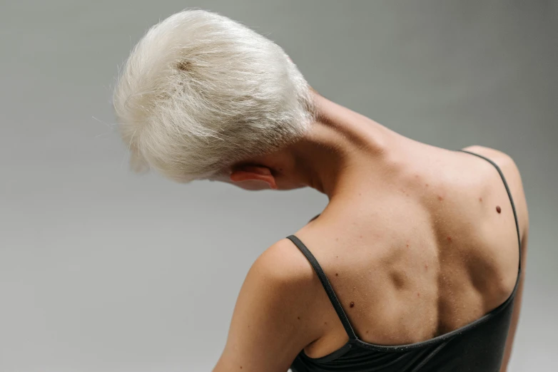 a woman in a black dress holding a cell phone, an album cover, trending on pexels, hyperrealism, short white hair shaved sides, bare back, wrinkled muscles skin, silver hair (ponytail)