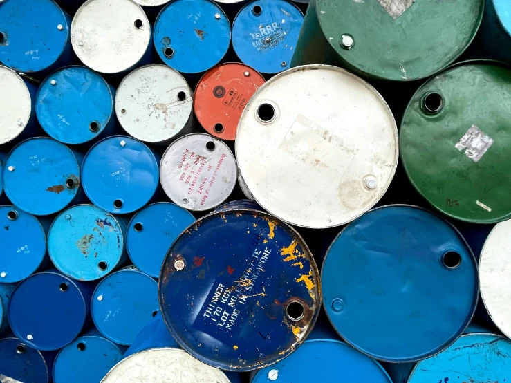 a bunch of barrels sitting next to each other, an album cover, unsplash, process art, brand colours are green and blue, mining scrap metal, shipping containers, petrol energy