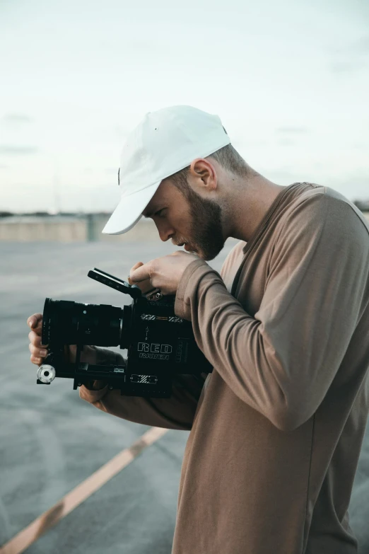 a man holding a camera in front of a body of water, movie cinematography, looking down on the camera, tv production, unsplash photography