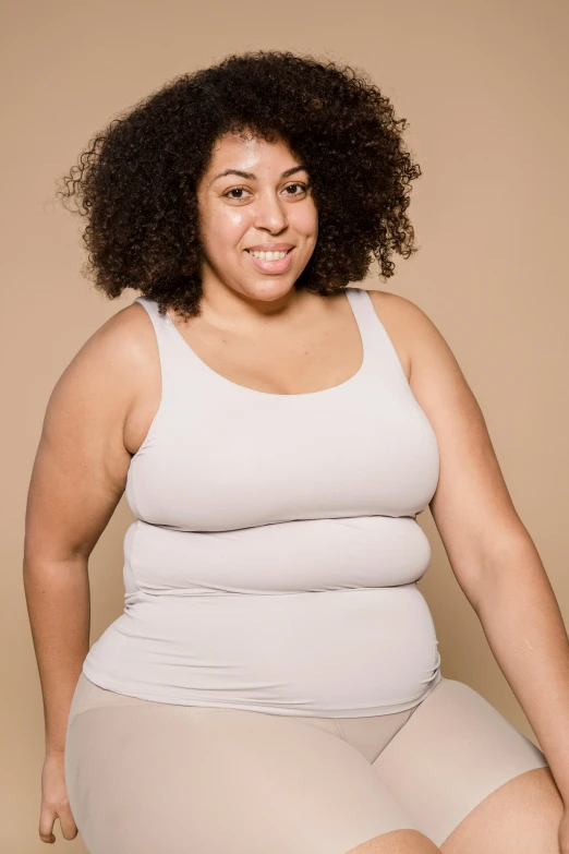 a woman in a white tank top sitting on a stool, plus-sized, light-brown skin, big complex belly mechanism, plain background