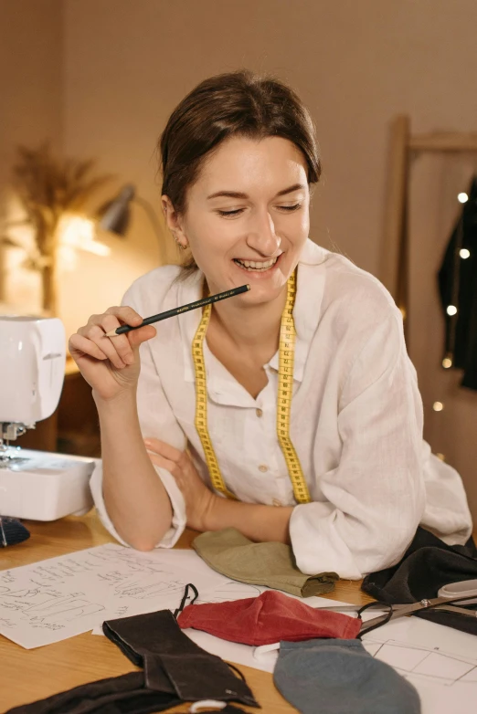 a woman sitting at a table in front of a sewing machine, a drawing, pexels contest winner, earing a shirt laughing, holding pencil, fancy dressing, premium quality