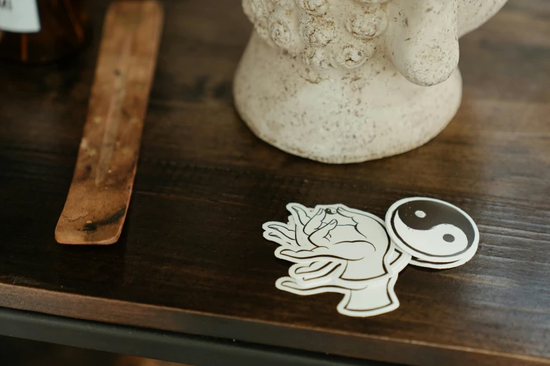 a statue sitting on top of a wooden table, a tattoo, inspired by Wu Wei, trending on pexels, die cut sticker, white, yinyang shaped, product introduction photo