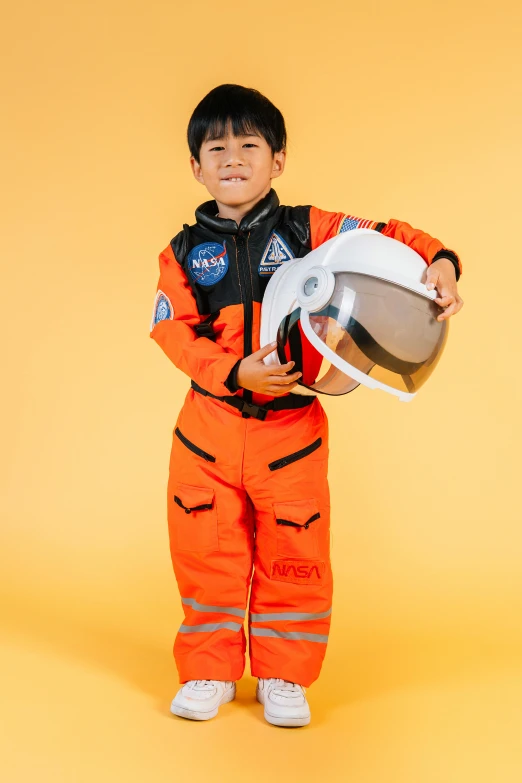 a young boy in an orange space suit holding a helmet, trending on unsplash, shin hanga, wearing human air force jumpsuit, photo from a promo shoot, ken wong, ross tan