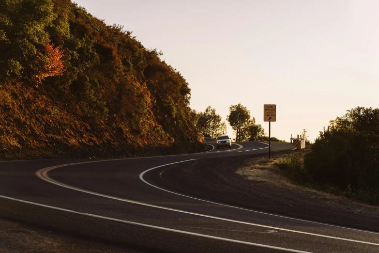 a couple of cars driving down a curvy road, by Lee Loughridge, unsplash contest winner, late summer evening, lachlan bailey, hillside, side