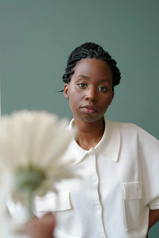 a woman standing in front of a mirror holding a flower, by Dulah Marie Evans, wearing a white button up shirt, adut akech, sitting on a mocha-colored table, hammershøi