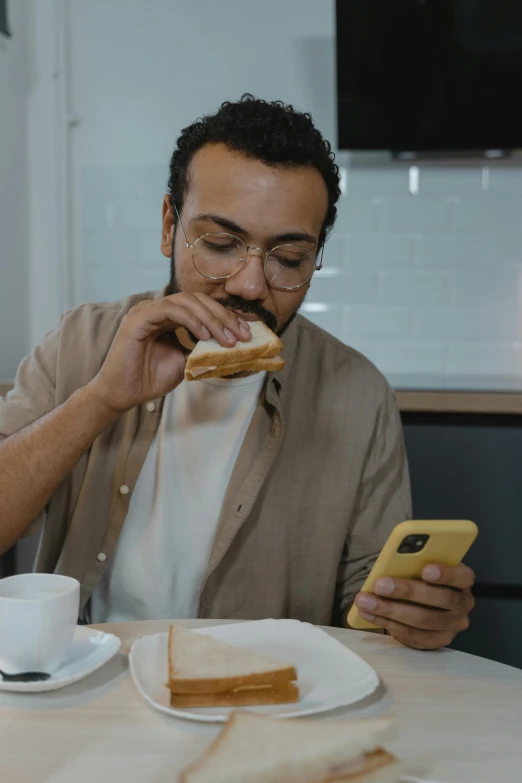 a man sitting at a table eating a sandwich, a photo, trending on pexels, holding a very advance phone, avatar image, riyahd cassiem, profile image