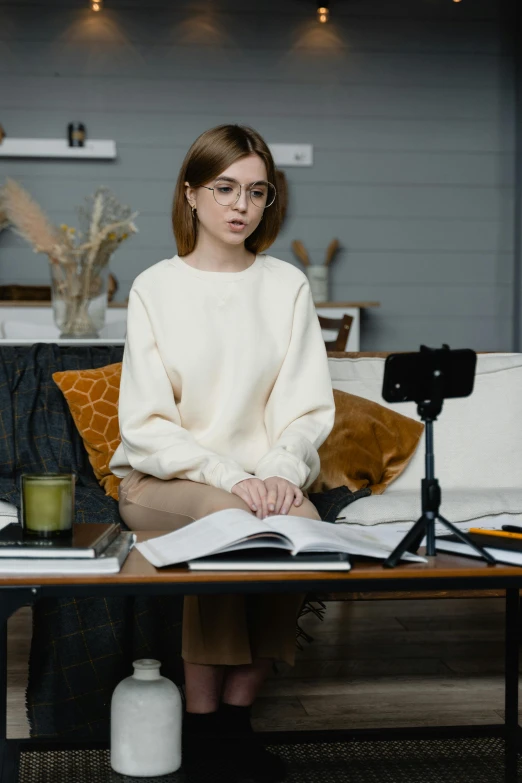 a woman sitting on a couch reading a book, a portrait, trending on pexels, standing on a desk, movie photo, wearing a white sweater, avatar image