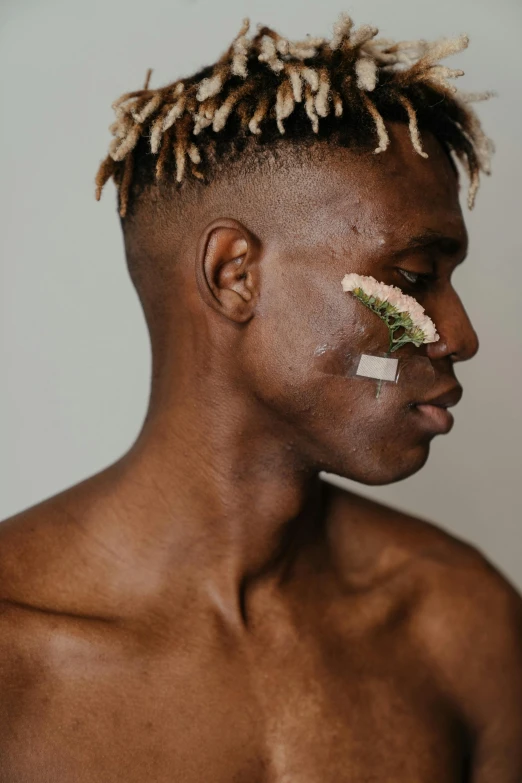 a man with a piece of tape on his face, by Cosmo Alexander, trending on pexels, afrofuturism, dark green leaf hair, delicate androgynous prince, flowers growing out of his body, messy blond hair