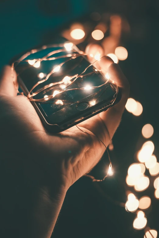a person holding a cell phone in their hand, by Adam Marczyński, pexels, fairy lights, bedazzled, simplistic, instagram post