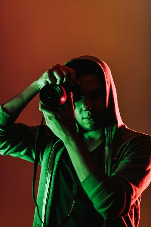 a man taking a picture with a camera, red and green lighting, wearing a dark hood, serious composure, stockphoto