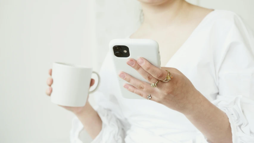 a woman holding a cup and a cell phone, inspired by L. A. Ring, trending on pexels, glossy white metal, gold and white, pale milky white porcelain skin, 10k