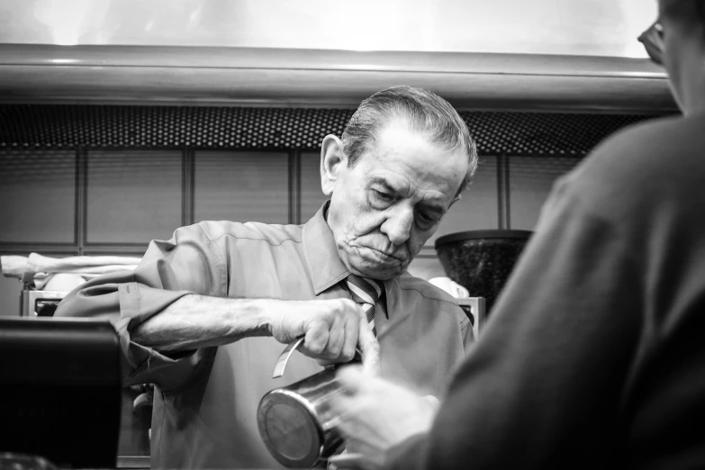 a black and white photo of a man in a kitchen, a black and white photo, by Alejandro Obregón, old man doing hard work, tailored clothing, combover, looking in mirror at older self