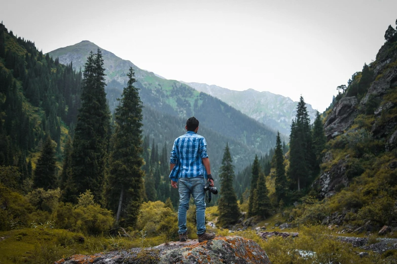 a man standing on top of a rock in the middle of a forest, pexels contest winner, an arab standing watching over, avatar image, hiking clothes, colored photo