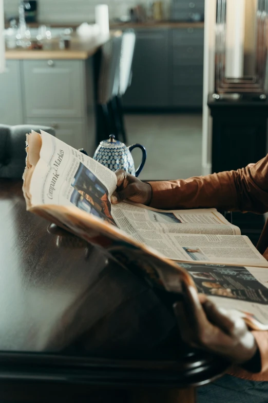 a woman sitting at a table reading a newspaper, by Sebastian Spreng, pexels contest winner, on a coffee table, thumbnail, brown, asian man