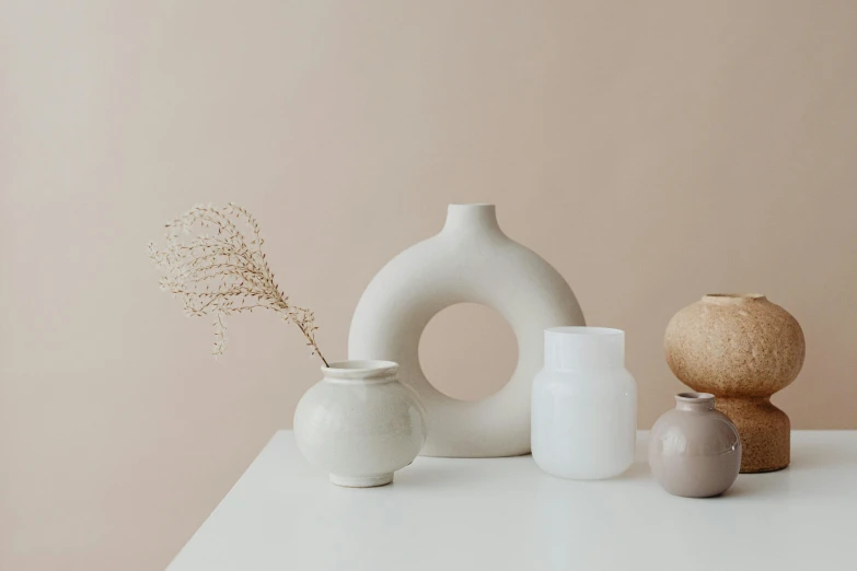 a group of vases sitting on top of a white table, trending on unsplash, minimalism, beige mist, background image, white sweeping arches, jar on a shelf