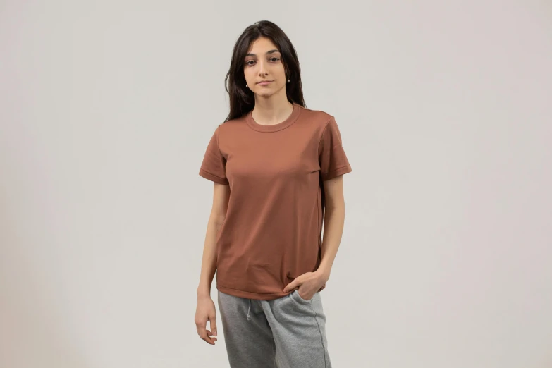 a woman standing with her hands in her pockets, a portrait, unsplash, brown shirt, sport t-shirt, front profile shot, dezeen