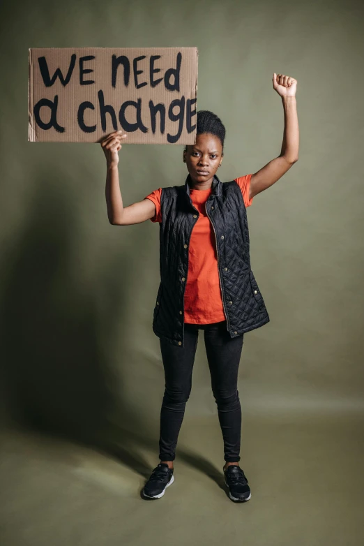 a woman holding a sign that says we need change, an album cover, by Ingrida Kadaka, trending on unsplash, black arts movement, fullbody or portrait, studio picture, portrait n - 9, an angry