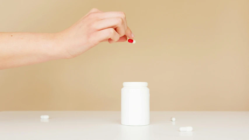 a person taking a pill out of a bottle, by Nicolette Macnamara, unsplash, antipodeans, on a white table, instagram post, plain background, smooth porcelain skin