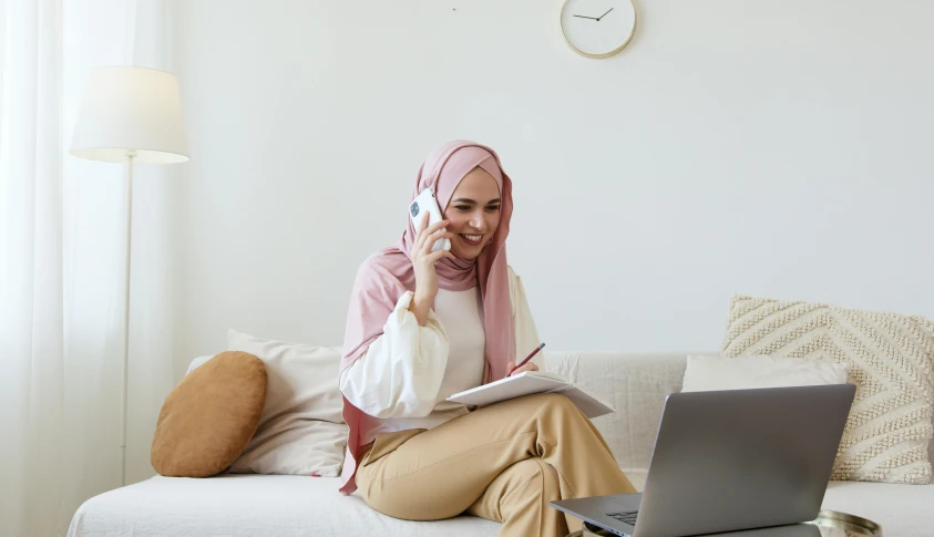 a woman sitting on a couch talking on a cell phone, inspired by Maryam Hashemi, trending on pexels, hurufiyya, white and pink cloth, sitting at a computer, malaysian, decorative