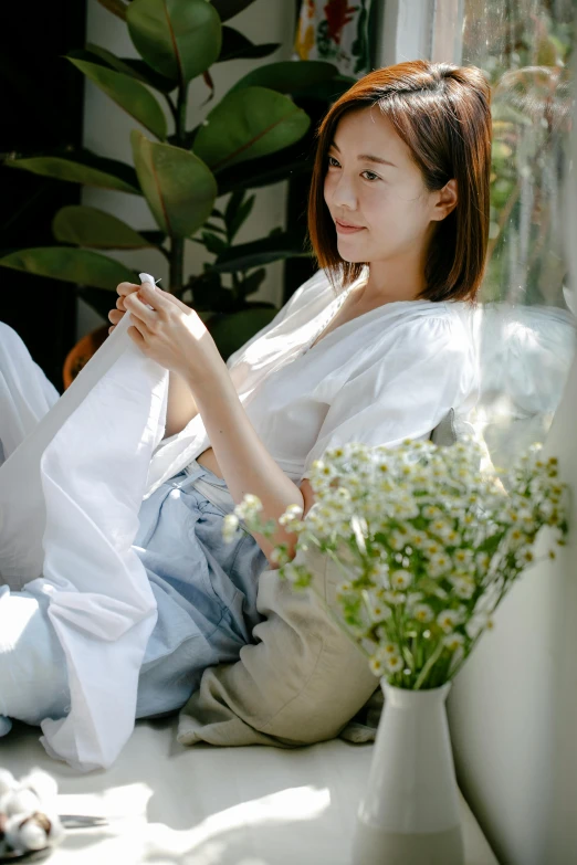 a woman sitting on a window sill reading a book, inspired by Cui Bai, wearing white shirt, touching her clothes, holding flowers, at the sitting couch