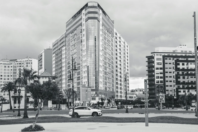 a black and white photo of a city street, by Luis Molinari, pexels contest winner, modernism, multistory building, car shot, near the beach, capital plaza