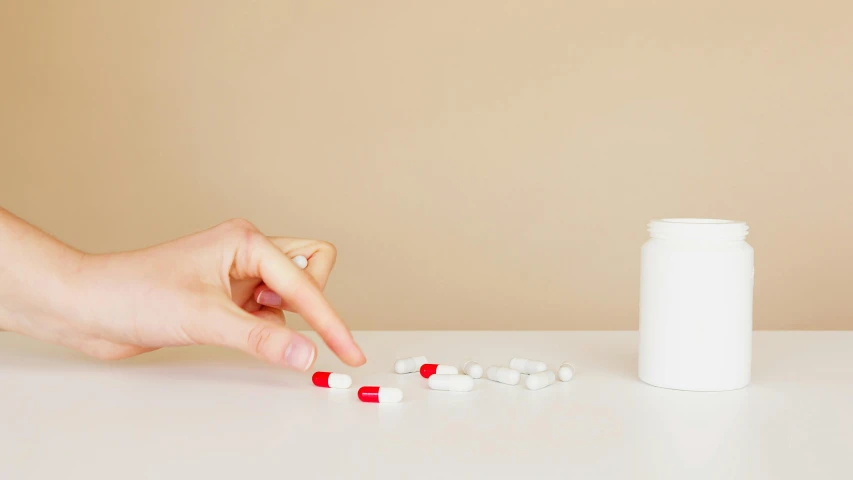 a person taking pills from a bottle on a table, by Gavin Hamilton, unsplash, antipodeans, plain background, white, ultrarealistic, hand