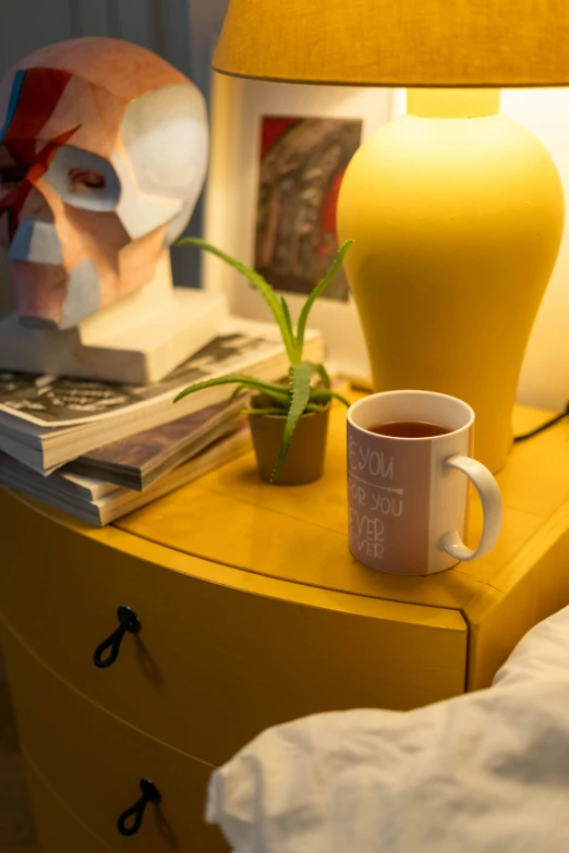 a yellow nightstand with a cup of coffee on it, inspired by Wes Anderson, featured on reddit, photorealism, detailed ambient lighting, tea cup, angle view, next to a plant