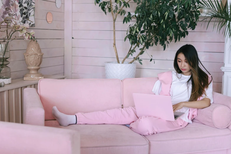 a woman sitting on a pink couch using a laptop, inspired by helen huang, trending on pexels, aestheticism, wearing a tracksuit, elves sitting on the couch, vietnamese woman, white and pink cloth