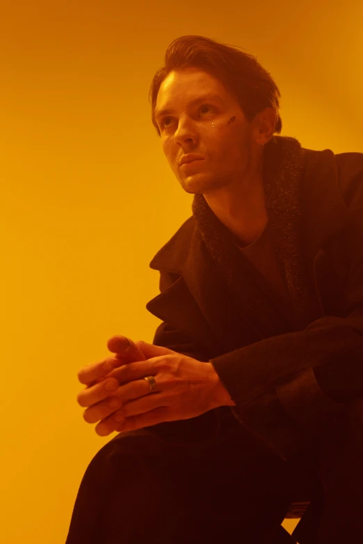 a man sitting on a chair in a yellow room, an album cover, unsplash, bauhaus, tobey maguire, orange glow, thin young male, washed out