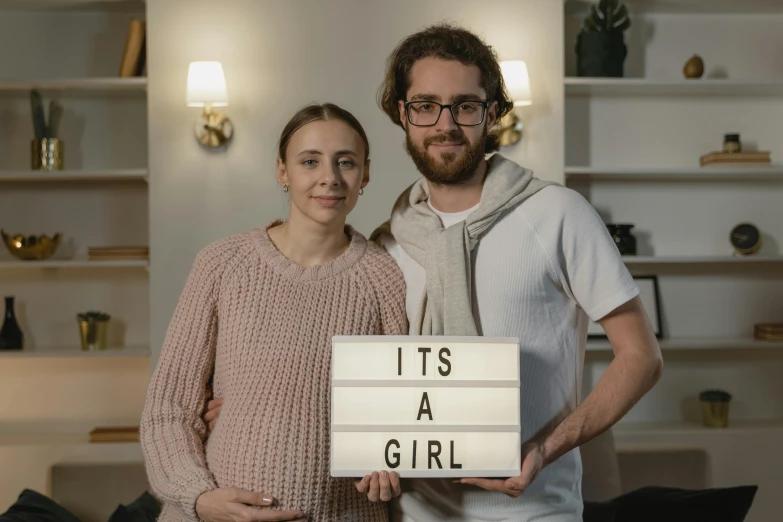 a man and a woman holding a sign that says it's a girl, a picture, pexels contest winner, serial art, light box, hyperrealistic image, at home, mid 2 0's female
