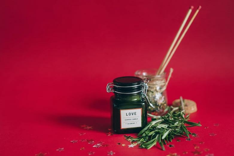 a jar of olive oil next to a sprig of rosemary, a still life, inspired by Marina Abramović, unsplash, on a red background, candle, incense, miniature product photo