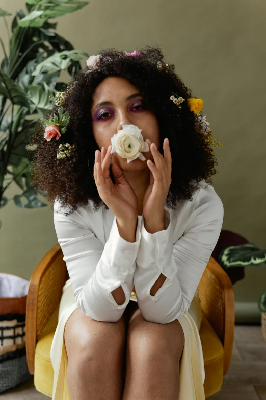 a woman sitting on a chair with a flower in her hair, trending on pexels, renaissance, curly afro, hand over mouth, an all white human, made of dried flowers