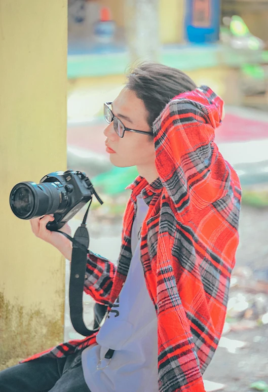 a woman sitting on a bench holding a camera, wearing a scarlet hoodie, in style of lam manh, colorful photograph, photography]