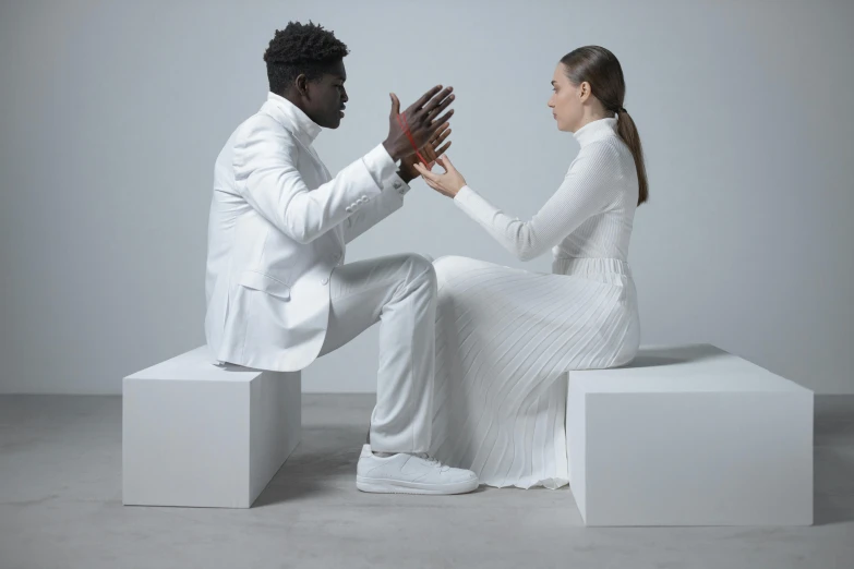 a man and woman sitting on cubes giving each other a high five, an album cover, inspired by David Bailly, pexels contest winner, romanticism, white suit, adut akech, showstudio, on a white table