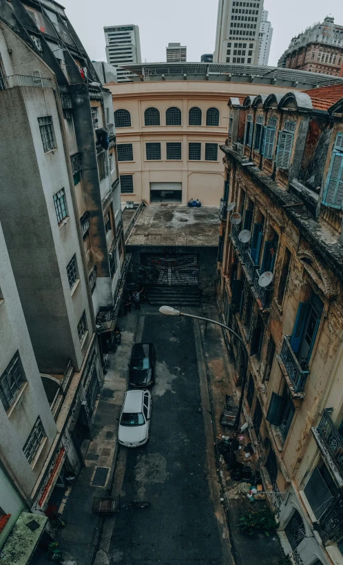 a white van driving down a street next to tall buildings, pexels contest winner, street art, high view, an abandonded courtyard, colonial era street, hong kong buildings