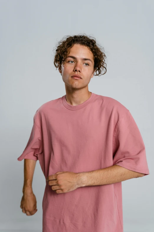 a man in a pink t - shirt poses for a picture, an album cover, trending on unsplash, non binary model, cropped wide sleeve, ryan dyar, frank dillane