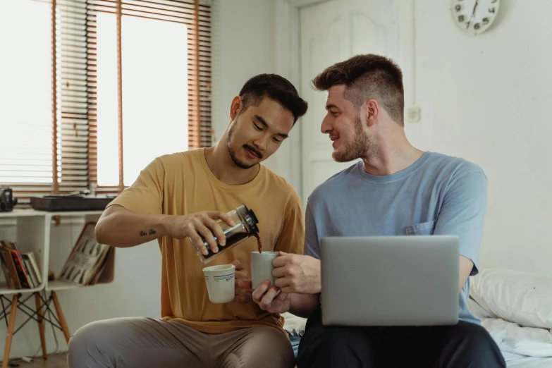 a couple of men sitting on top of a bed next to each other, pexels contest winner, aussie baristas, programming, is ((drinking a cup of tea)), gay