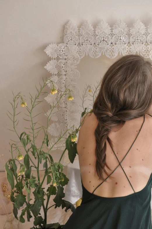 a woman in a green dress standing in front of a mirror, inspired by Elsa Bleda, trending on pexels, renaissance, bare back, hair : long brown, adorned with all kind of plants, wearing white camisole