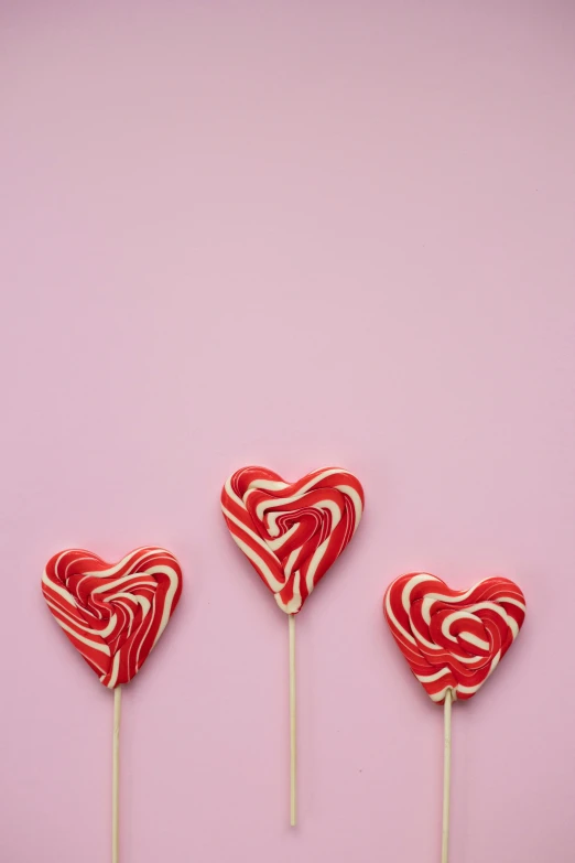 three lollipops in the shape of hearts on a pink background, by Valentine Hugo, pexels, food styling, red and white stripes, 15081959 21121991 01012000 4k, square