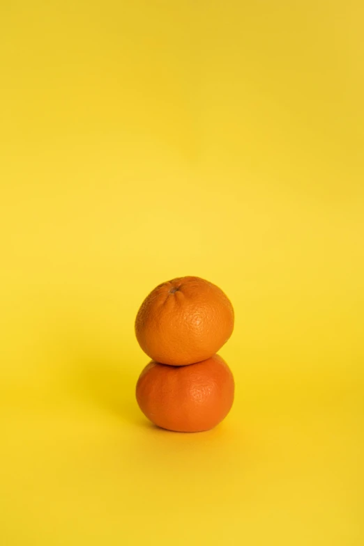 two oranges stacked on top of each other on a yellow background, a still life, pexels contest winner, two still figures facing camera, without text, set against a white background, unedited