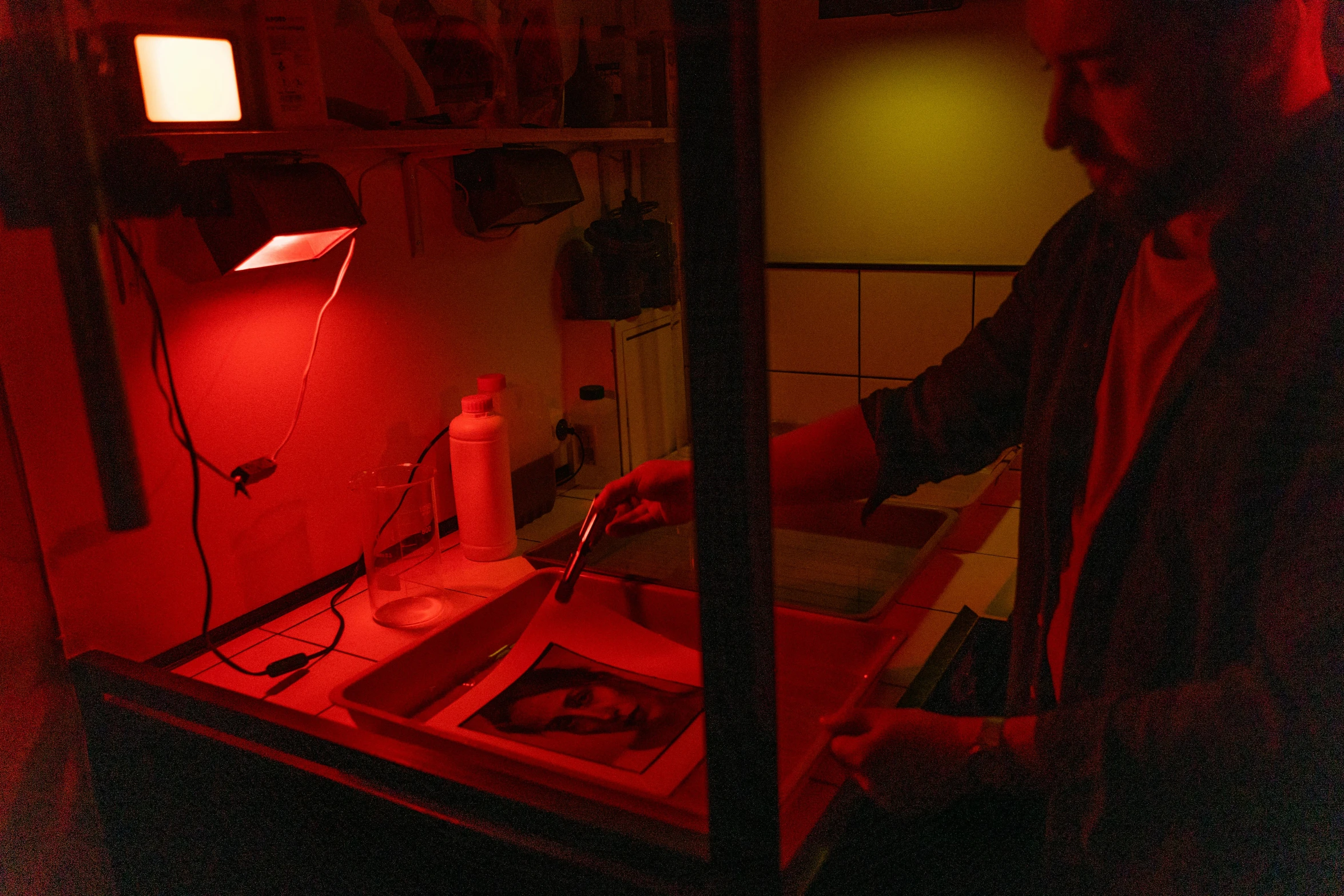 a man standing in front of a red light, a silk screen, in a lab, vivarium, dye contrast lighting, digging