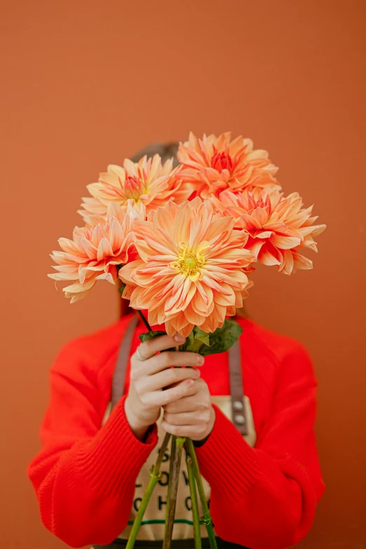 a person holding a bunch of flowers in front of their face, orange color theme, dahlias, understated, looking straight