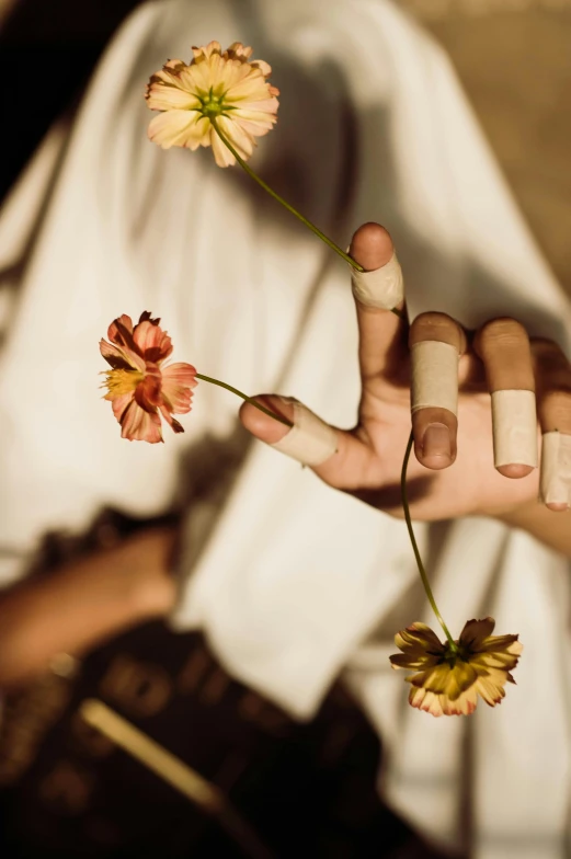 a close up of a person holding a flower, inspired by Elsa Bleda, aestheticism, bandage taped fists, earthy tones, long fingers, woman holding another woman