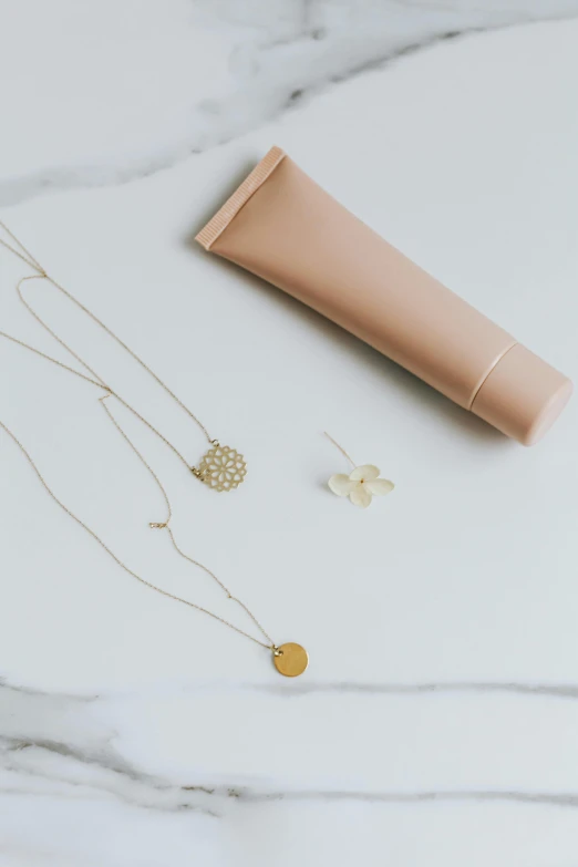 a bottle of sunscreen sitting on top of a marble counter, inspired by Eden Box, minimalism, wearing several pendants, gold flowers, muted color. minimalist, golden ratio jewelry candy