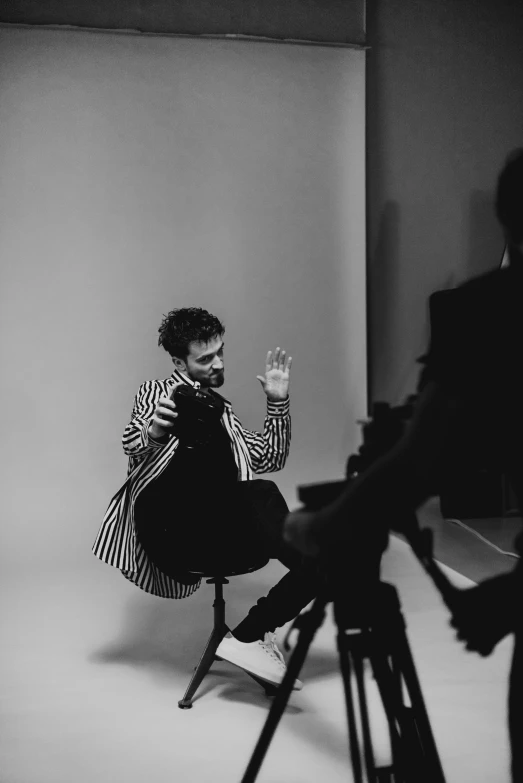 a woman sitting on a chair in front of a camera, a black and white photo, unsplash, robert sheehan, wearing a fancy jacket, mana shooting from his hands, video footage