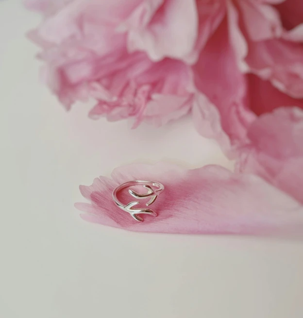a silver ring sitting on top of a pink flower, on a white table