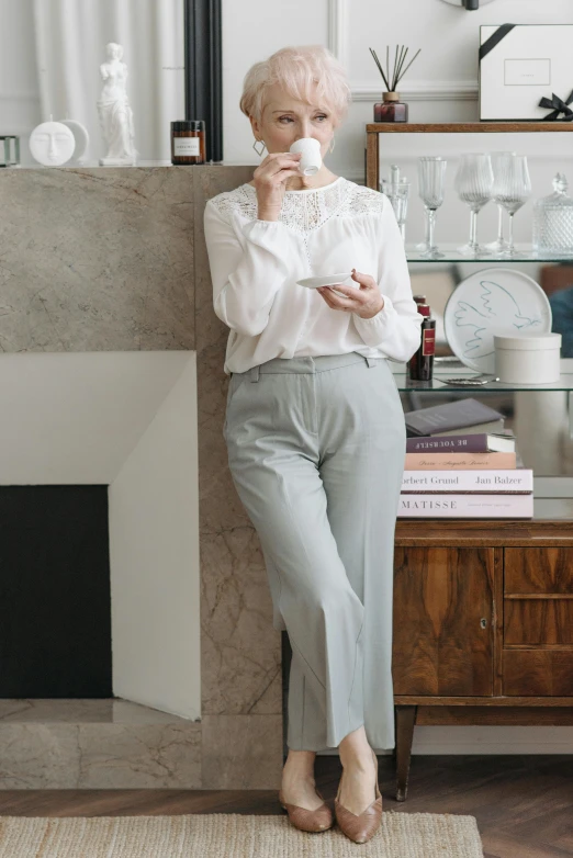 a woman standing next to a fireplace in a living room, inspired by Ramon Pichot, instagram, wearing a light blue shirt, on a white table, formal attire, light grey mist