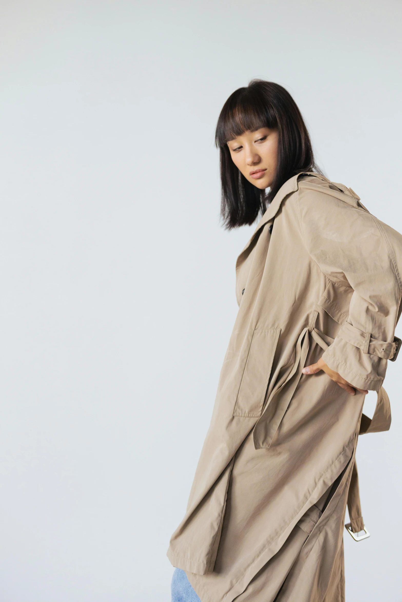 a woman standing in front of a white wall, an album cover, by Miyamoto, unsplash, mingei, light brown trenchcoat, model エリサヘス s from acquamodels, sustainable materials, ethnicity : japanese