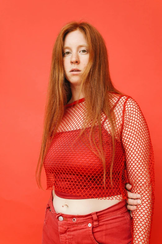 a woman standing in front of a red wall, an album cover, inspired by Julia Pishtar, renaissance, red mesh in the facede, wearing a cropped top, hr ginger, candid portrait photo