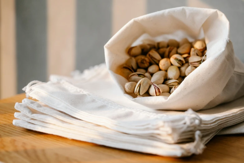 a bag filled with nuts sitting on top of a wooden table, inspired by Károly Patkó, unsplash, private press, ecru cloth, striped, close-up product photo, alternate angle